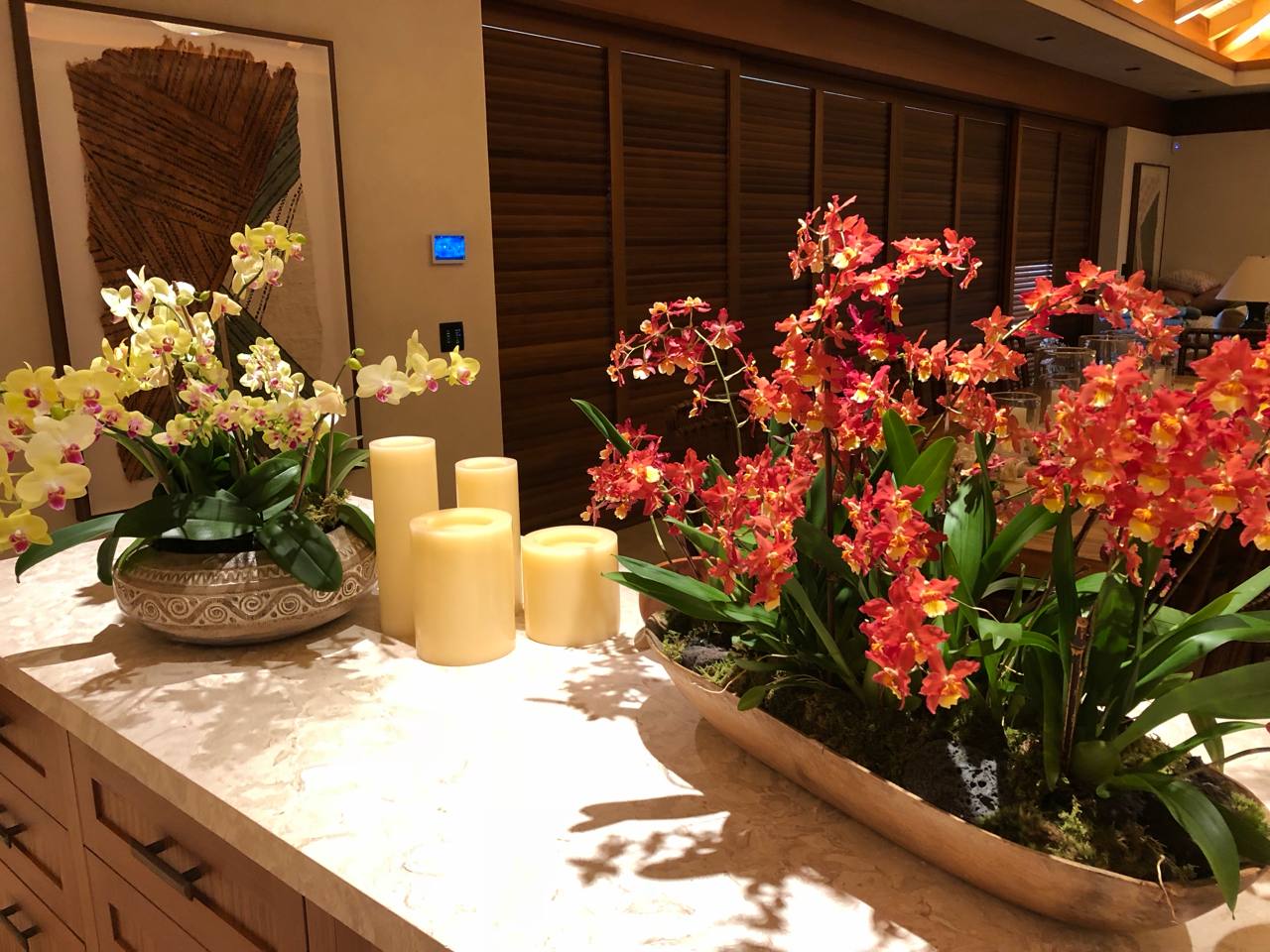 Control4 touchscreen beside orchids and koa wood shutters — technology invisible in a luxury Kukio home