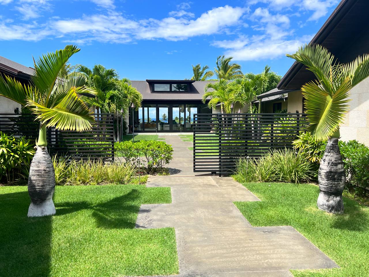 Contemporary Hawaiian estate — bottle palms, black slat gate, SmartHomes.us