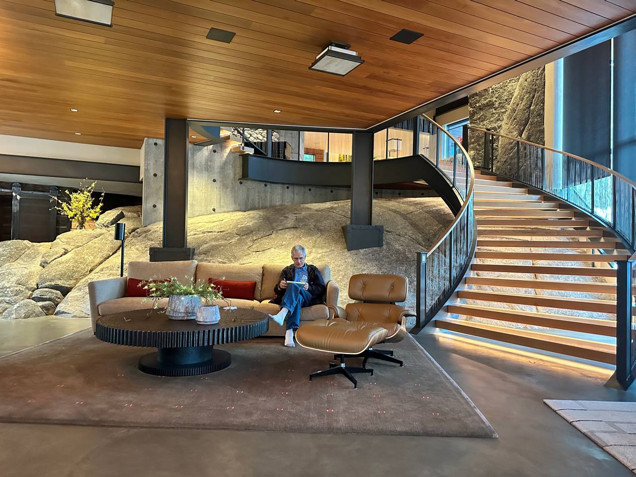 McCall Idaho — living room built into rock, curved staircase, glass railing, Eames chair, boulders