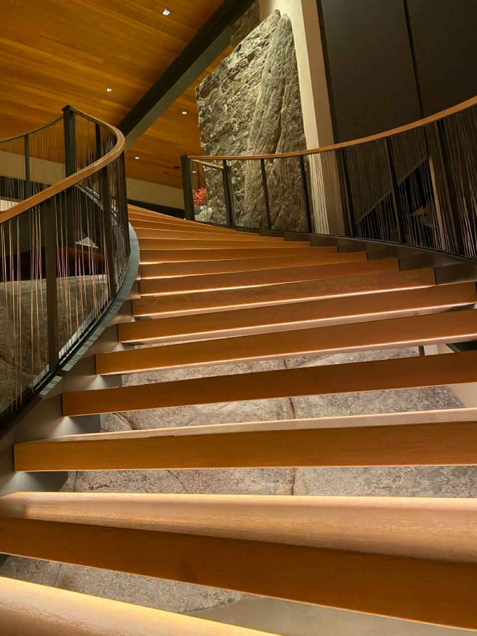 McCall Idaho — curved staircase with LED-lit treads, stone risers, rock face, wood ceiling