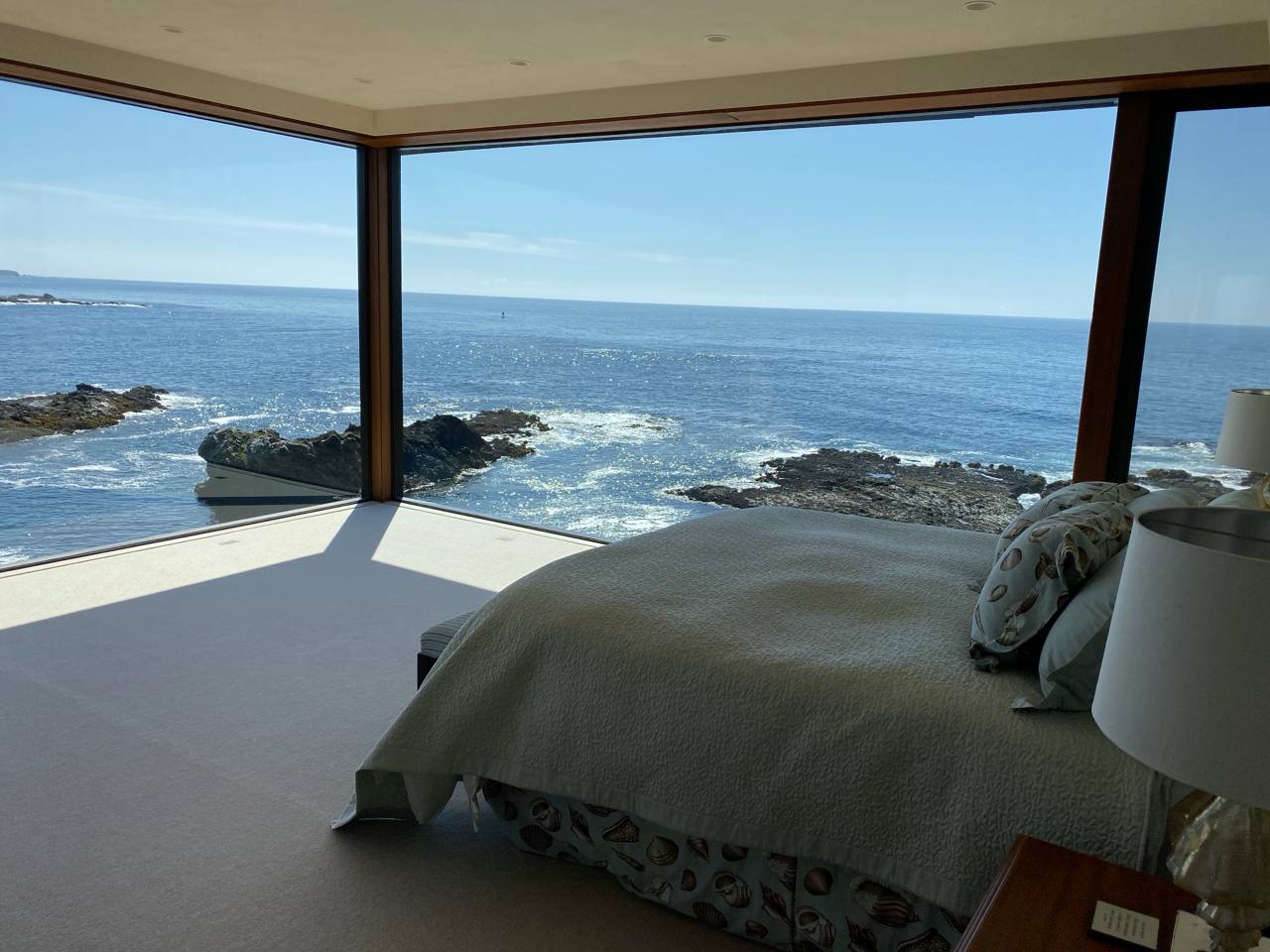 Oceanfront bedroom — corner windows, Pacific sunlight, sage coverlet, lava rock shore