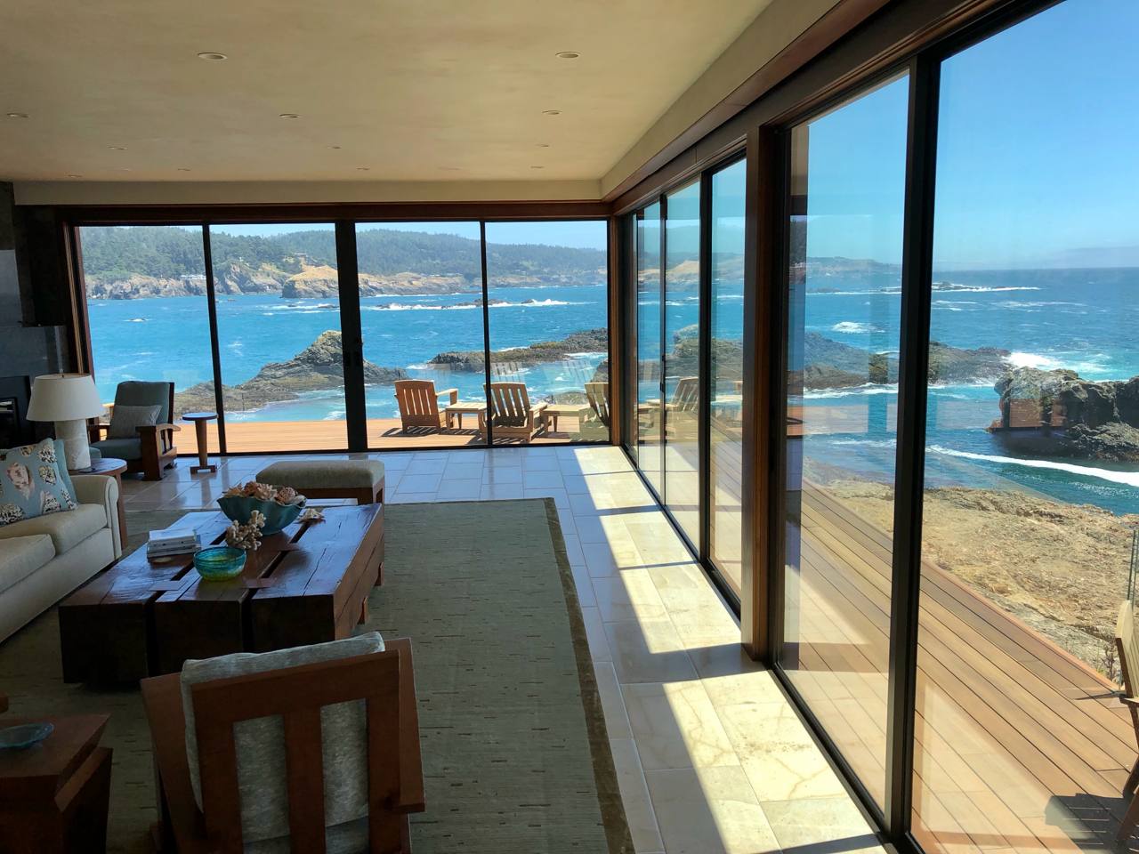 Oceanfront living room — floor-to-ceiling glass, lava rock coastline