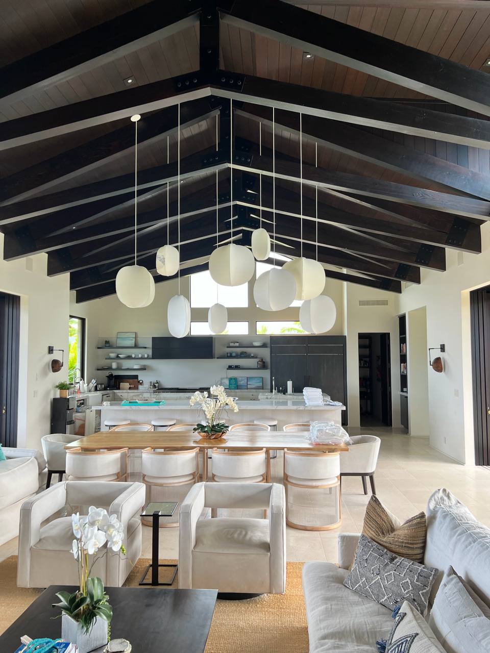 Open-concept great room — vaulted koa beams, pendant lanterns, kitchen island, orchids