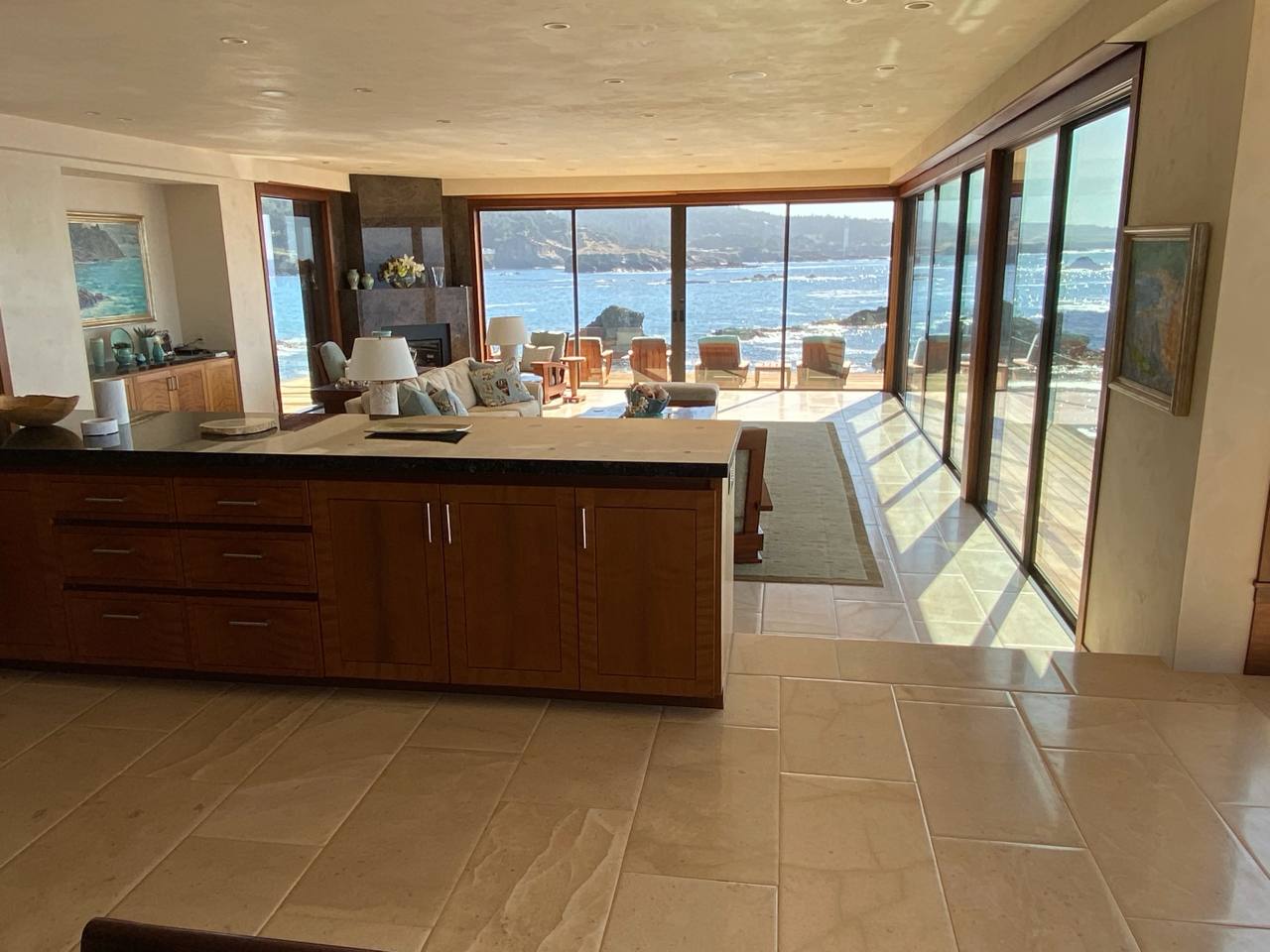 Open-concept kitchen and living — sliding glass, rocky shoreline, sunlight shadows on stone