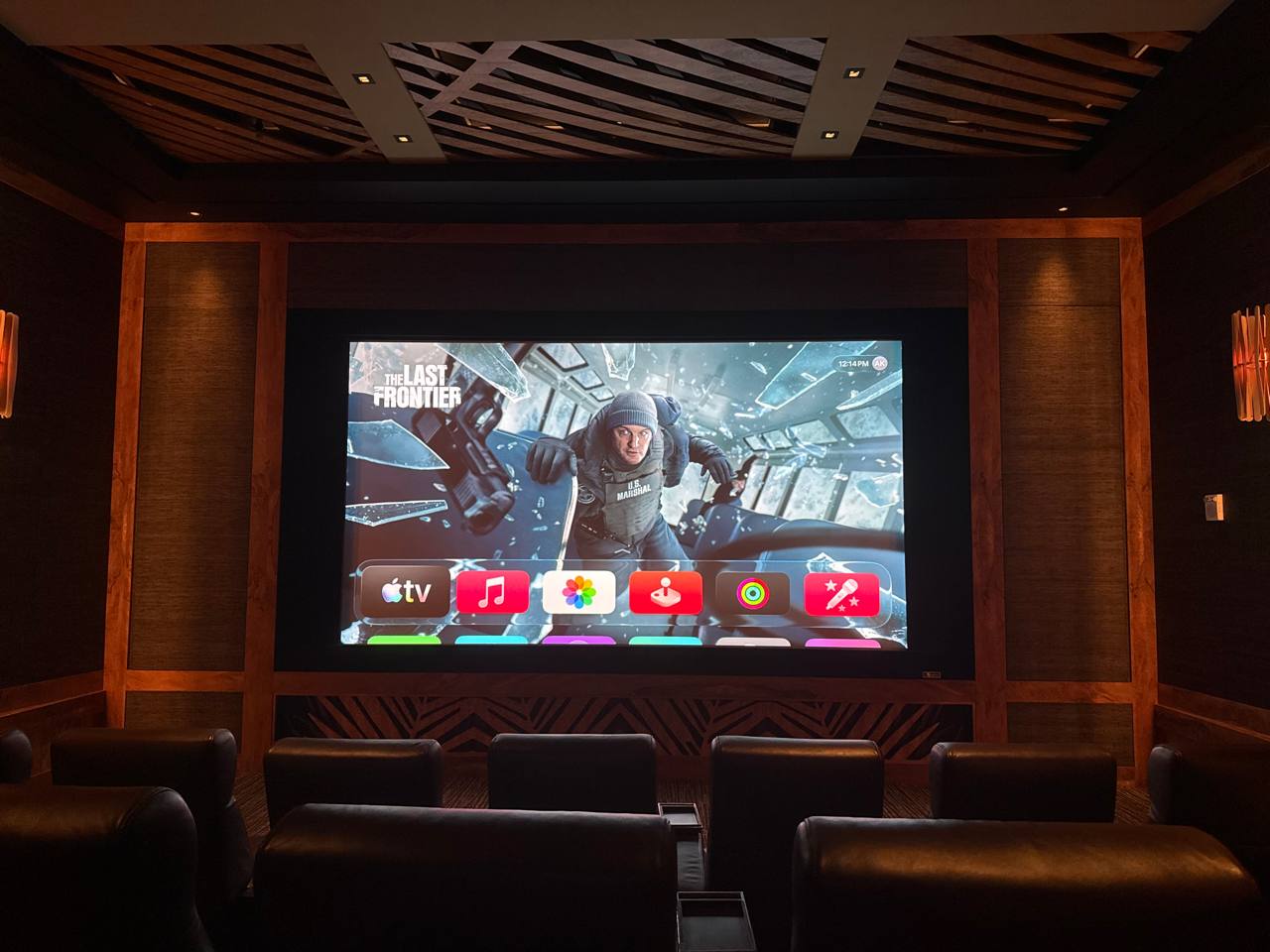 Private home cinema by SmartHomes.us — dark wood paneling, acoustic ceiling, projection screen, leather recliners