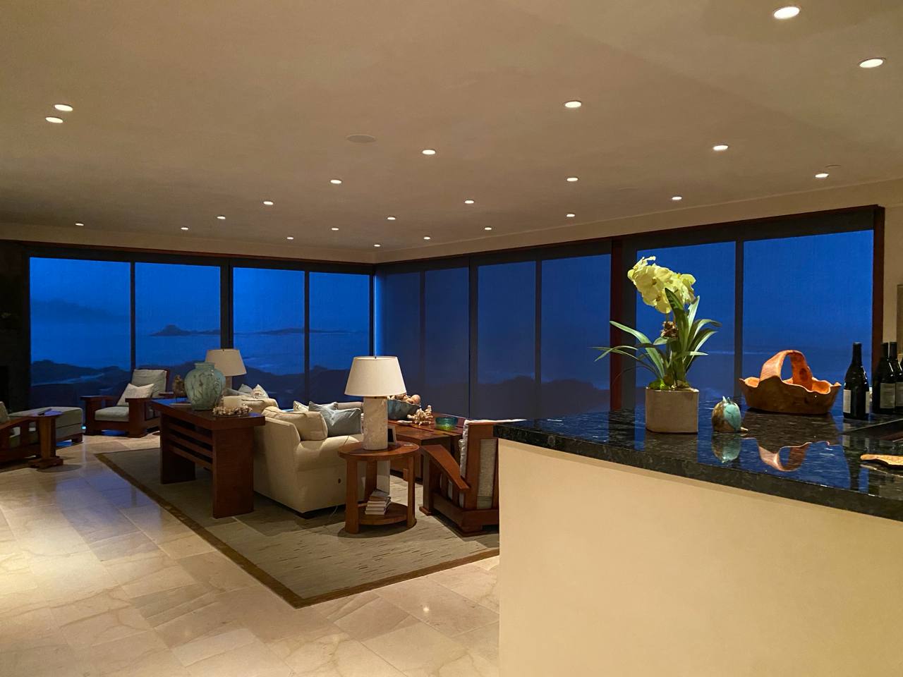 Twilight living room — cream sofas, orchid, ocean and island view at dusk